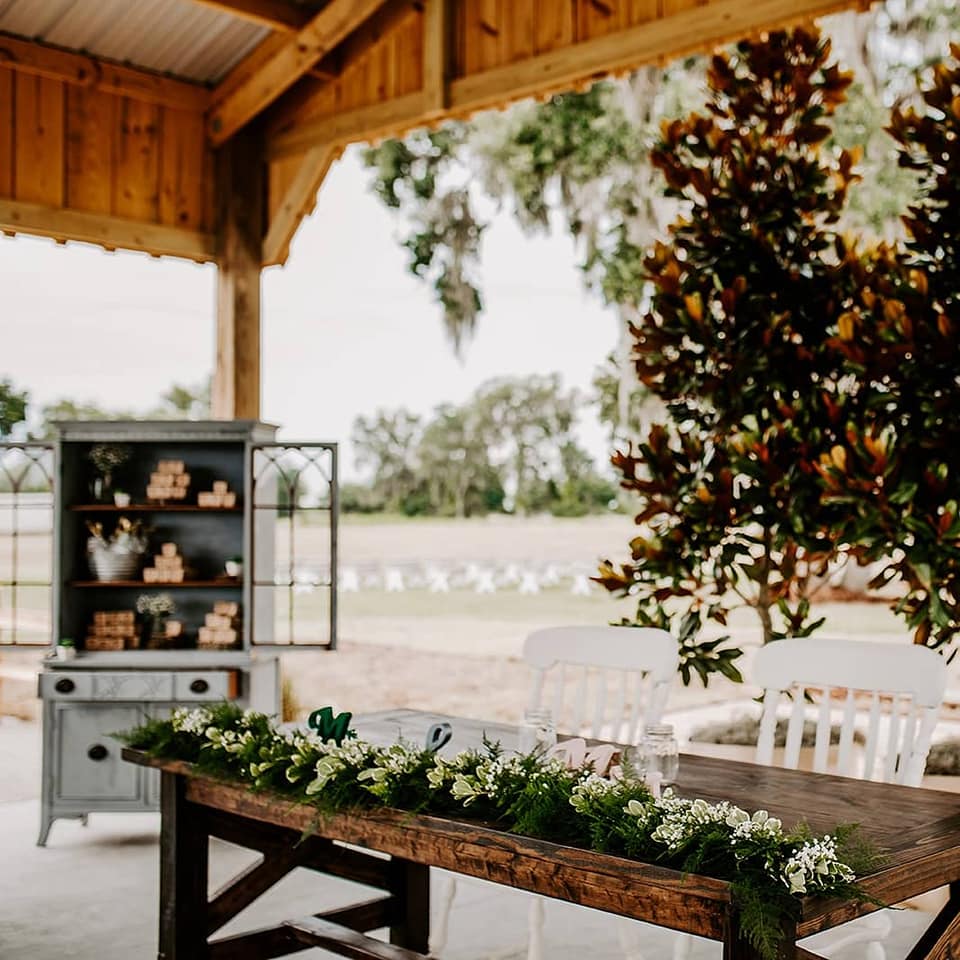 open air barn set up for wedding with sweetheart table with green and white garland